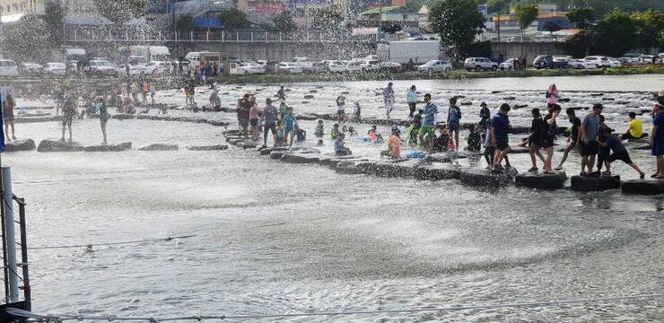 장흥 탐진강변에서 사람들이 분수처럼 내리는 물을 맞으며 걷고 있는 모습