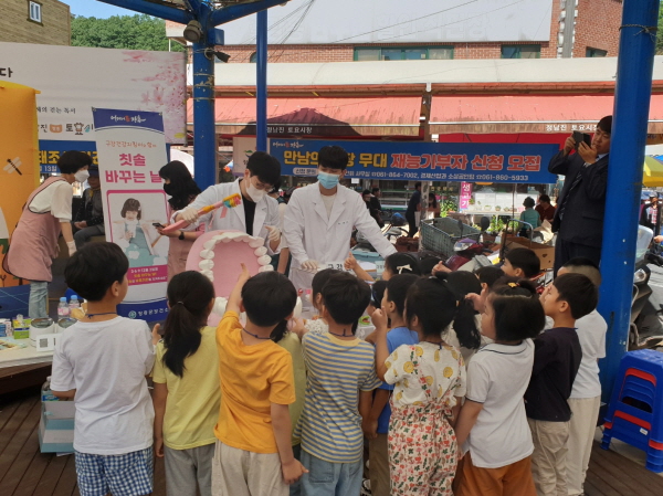 토요시장에서 구강보건의 날 행사 모습 - 보건소 직원들이 어린이들에게 올바른 칫솔질 방법을 치아 모형으로 설명하는 모습