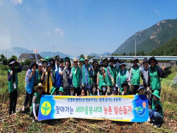 장흥군 새마을회 회원들과 직장·공장새마을운동 장흥군협의회 회원들이 마늘밭앞에서 현수막(상생과 협력으로 만들어가는 함께 잘사는 공동체 찾아가는 새마을 봉사대 농촌일손돕기)을 들고 단체기념촬영을 하는 모습